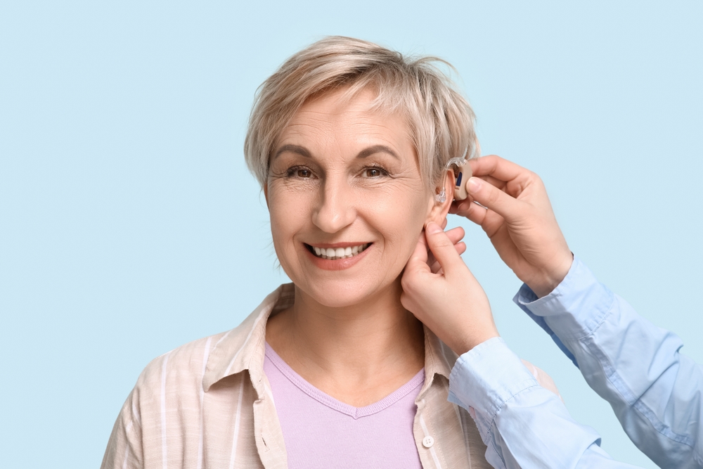 Young,Woman,Putting,Hearing,Aid,In,Mature,Woman's,Ear,On